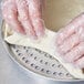 A person's hands in plastic gloves using an American Metalcraft Super Perforated Pizza Pan to make dough.