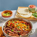 A pan of Eat Meati plant-based carne asada steak with vegetables next to a bowl of tortillas on a table.