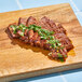 Sliced Eat Meati plant-based carne asada steak on a wooden surface with herbs.