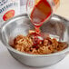 A bowl filled with Sweet Baby Ray's Sweet 'n Spicy BBQ Sauce with a spoon.