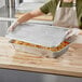 A woman in an apron holding a Choice heavy-duty foil steam table pan full of food.