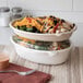 An oval-shaped, compostable sugarcane bowl filled with salad, shown stacked on another bowl with a clear lid.