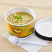 A bowl of soup with a spoon and a white plastic lid.