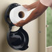 A hand holding a black roll of San Jamar EcoLogic jumbo toilet paper.