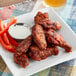 A plate of chicken wings and vegetables with a bowl of white dip.