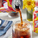 A can of Goya Tropi-Cola pouring into a glass of brown liquid with ice.