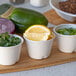 A small white compostable sugarcane portion cup filled with lemon wedges, shown alongside other portion cups with herbs and vegetables.