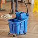 A man using a Carlisle blue mop bucket with wringer on wheels.