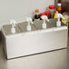 A Carlisle stainless steel condiment dispenser rail with white plastic pumps on a counter.