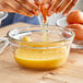 A person breaking an egg into a glass bowl of eggs.