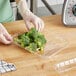 A person in gloves using a plastic tray to hold cut broccoli.