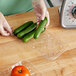 A person holding a clear plastic meat tray of cucumbers.