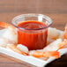 A plate of shrimp with Carlisle clear plastic sauce cups filled with red sauce.