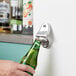 A hand using a Choice stainless steel mounted bottle opener to open a green bottle.