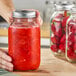 A person holding a Choice regular mouth glass canning jar filled with red liquid and a silver metal lid.