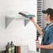 A man in a blue apron holding a pizza on a Regency stainless steel wall shelf.