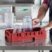 A man holding a red Cambro dish rack with clear glass cups.