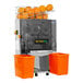 An Omcan automatic stainless steel juice extractor with oranges in it.