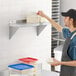 A man in a black apron reaching for food containers on a Regency stainless steel wall shelf.