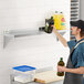 A man's hand holding a bottle of olive oil on a Regency stainless steel wall shelf.