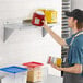 A man holding a yellow plastic container of ketchup and mustard on a Regency stainless steel wall shelf.