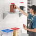 A man in a blue apron places food on a Regency stainless steel wall shelf in a professional kitchen.