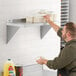 A man in a black shirt putting plates on a Regency stainless steel wall shelf.