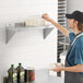 A man in an apron standing on a Regency stainless steel wall shelf holding a container.