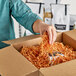 A person holding a box of Spring-Fill Cognac Crinkle Cut paper shred.