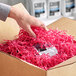 A hand holding a box of Spring-Fill Fuchsia Crinkle Cut paper shred with pink shredded paper inside.