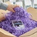 A person's hand holding a pile of Spring-Fill lavender shredded paper in a box.