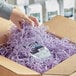 A hand holding a cardboard box filled with Spring-Fill Orchid Crinkle Cut paper shred in purple.