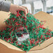 A hand using Spring-Fill Red and Green Crinkle Cut paper to pack a box.