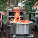 A couple of people sitting around a BREEO stainless steel fire pit with a fire burning.