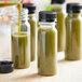 2 oz. Round Clear PET Tall Energy Bottles with Black Lids on a counter in a juice bar filled with green liquid.