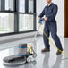 A man in a coverall using a Lavex Pro 20" dust-control burnisher on a floor.
