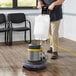 A man using a Lavex Pro floor machine to clean a hardwood floor in a professional kitchen.