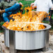 Two men sitting on a bench next to a BREEO stainless steel fire pit with flames.