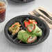 A black Ecopax 3-compartment plate of food with a drink.