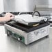 A person using a Waring panini grill on a stainless steel counter.