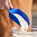 A hand holding a blue Vikan scoop pouring flour into a bowl.
