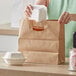 A woman using a Duro Kraft paper bag with die cut handles to put a white styrofoam container in.