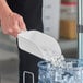 A hand holding a Vikan white polypropylene scoop of ice.