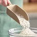 A person using a Vikan brown polypropylene hand scoop to scoop flour into a bowl.