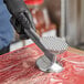 A person in black gloves using the Choice Dual-Sided Aluminum Meat Tenderizer on a piece of meat on a counter.