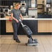 A woman using a NaceCare compact floor scrubber to clean a floor in a commercial space.