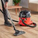 A person using a NaceCare canister vacuum to clean a wood floor.