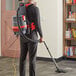 A man wearing a grey and red NaceCare backpack vacuum cleaner vacuuming the floor.