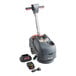 A NaceCare Solutions cordless walk behind floor scrubber with a black and red battery.