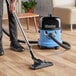 A person using a NaceCare wet/dry vacuum to clean a hardwood floor.